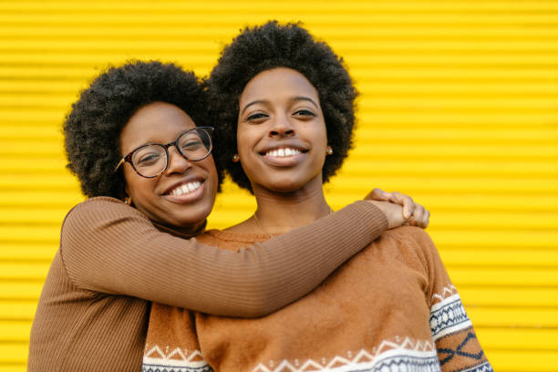 portrait-of-happy-twin-sisters-in-front-of-yellow-background