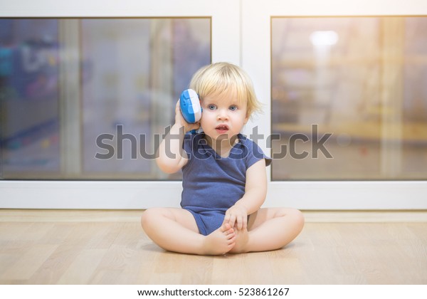 Portrait of a beautiful baby boy on the floor with music phone toys. 1,5 year-old child playing with educational cup toys at home. Little blond kid with blue eyes is playing with toy at home indoors